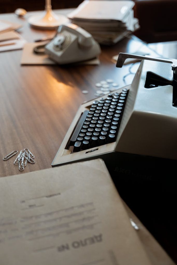 A vintage typewriter on a retro desk with documents and a rotary phone.